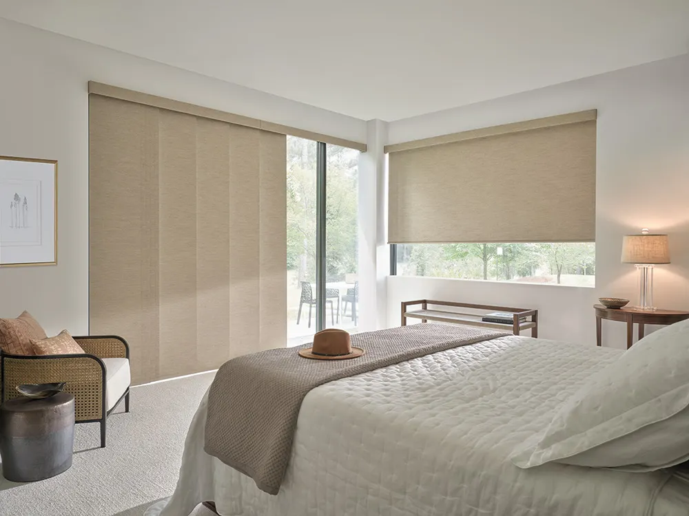 Bedroom with beige panel track blinds and a matching roller shade filtering soft daylight.